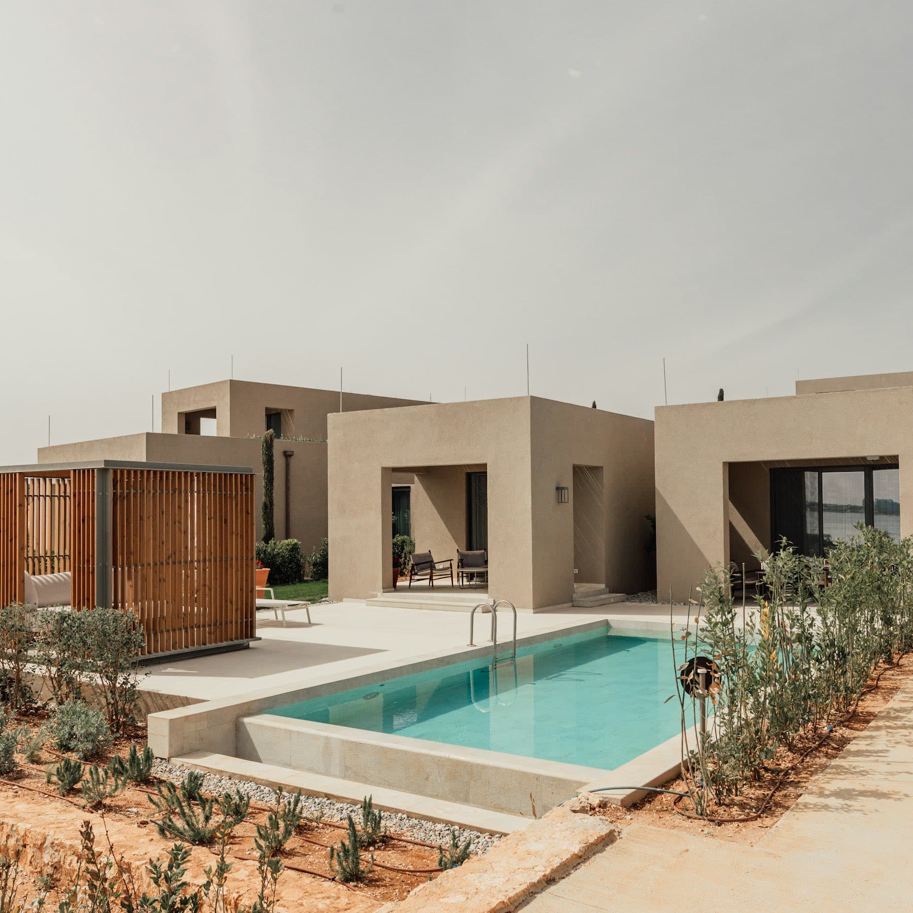Fachada de concreto y madera con alberca lateral entre vegetación